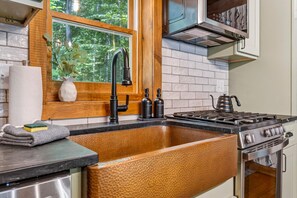 A kitchen with a large copper sink, a gas stove, and a window with a view of trees. - Family Retreat • Sauna • Hot Tub • Games • Peloton (Bartlett)