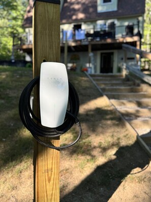 A Tesla charging station mounted on a wooden post with a house in the background. - Family Retreat • Sauna • Hot Tub • Games • Peloton (Bartlett)