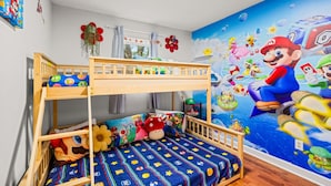 Een slaapkamer met stapelbed, een muurdecoratie met een Mario-thema, een houten kinderbedje en diverse speelgoed.