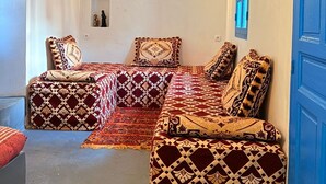 Un salón acogedor con un sofá modular, cojines estampados, una lámpara de pared y una puerta azul.