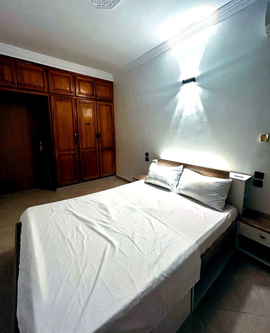 A bedroom with a bed, wooden wardrobe, and a nightstand.