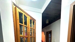 Un couloir avec une armoire en bois dotée de portes en verre, un sol carrelé et une porte donnant sur une autre pièce.
