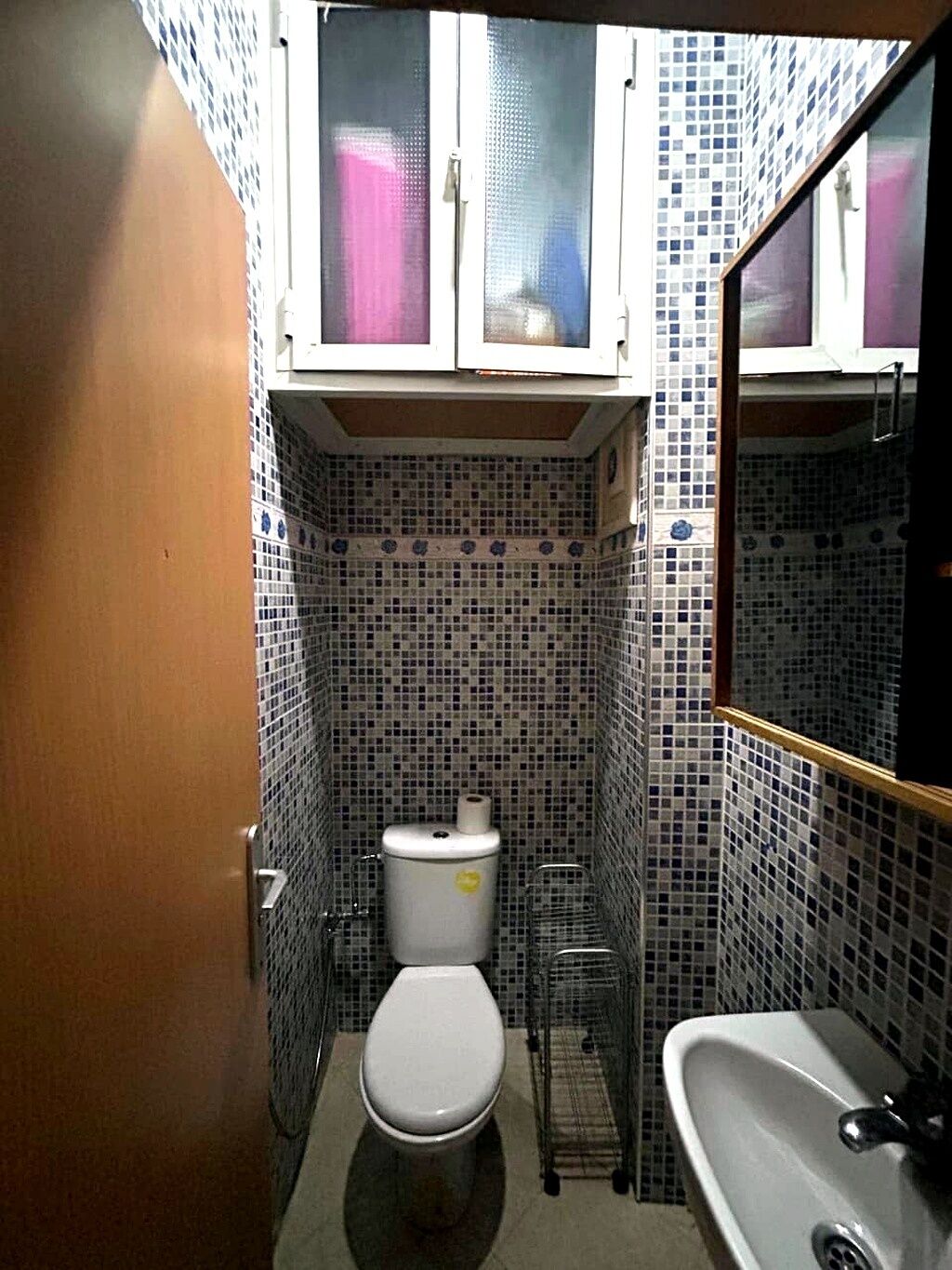 A compact bathroom with a toilet, sink, and tiled walls.