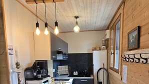 A compact kitchen with a stone island, wooden ceiling, and a stone wall backsplash.