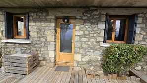 A stone building with a wooden door, two windows with wooden frames, and a small wooden bench outside.