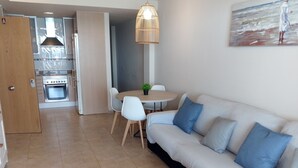 Ein modernes Wohnzimmer mit Sofa, Sesseln, einem Esstisch und einer Küchenzeile inklusive Herd und Backofen.