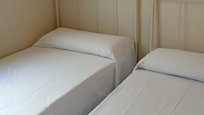 Zwei Einzelbetten mit weißer Bettwäsche in einem Raum mit schlichten Wänden und einem schlichten Metall-Kopfteil.
