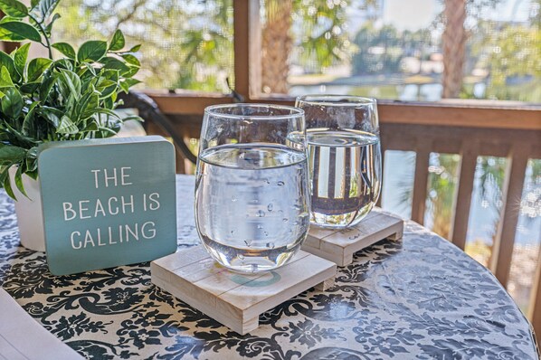 A table with three glasses of water, a sign reading "THE BEACH IS CALLING", and a potted plant.