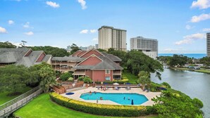 A hotel with a swimming pool, surrounded by lush greenery and a body of water.