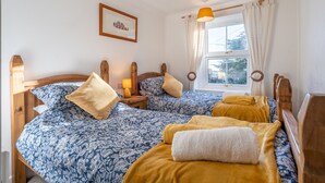 Ein Schlafzimmer mit zwei Holzbetten, einem fenster mit Vorhängen, einem gerahmten Bild an der Wand und einem Nachttisch mit Lampe.