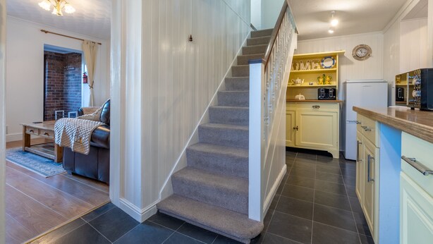 Eine Treppe führt zu einer zweiten Etage, eine Küche mit weißen Schränken und einem gelben Regal sowie ein Wohnbereich mit einer Couch und einem Kamin.