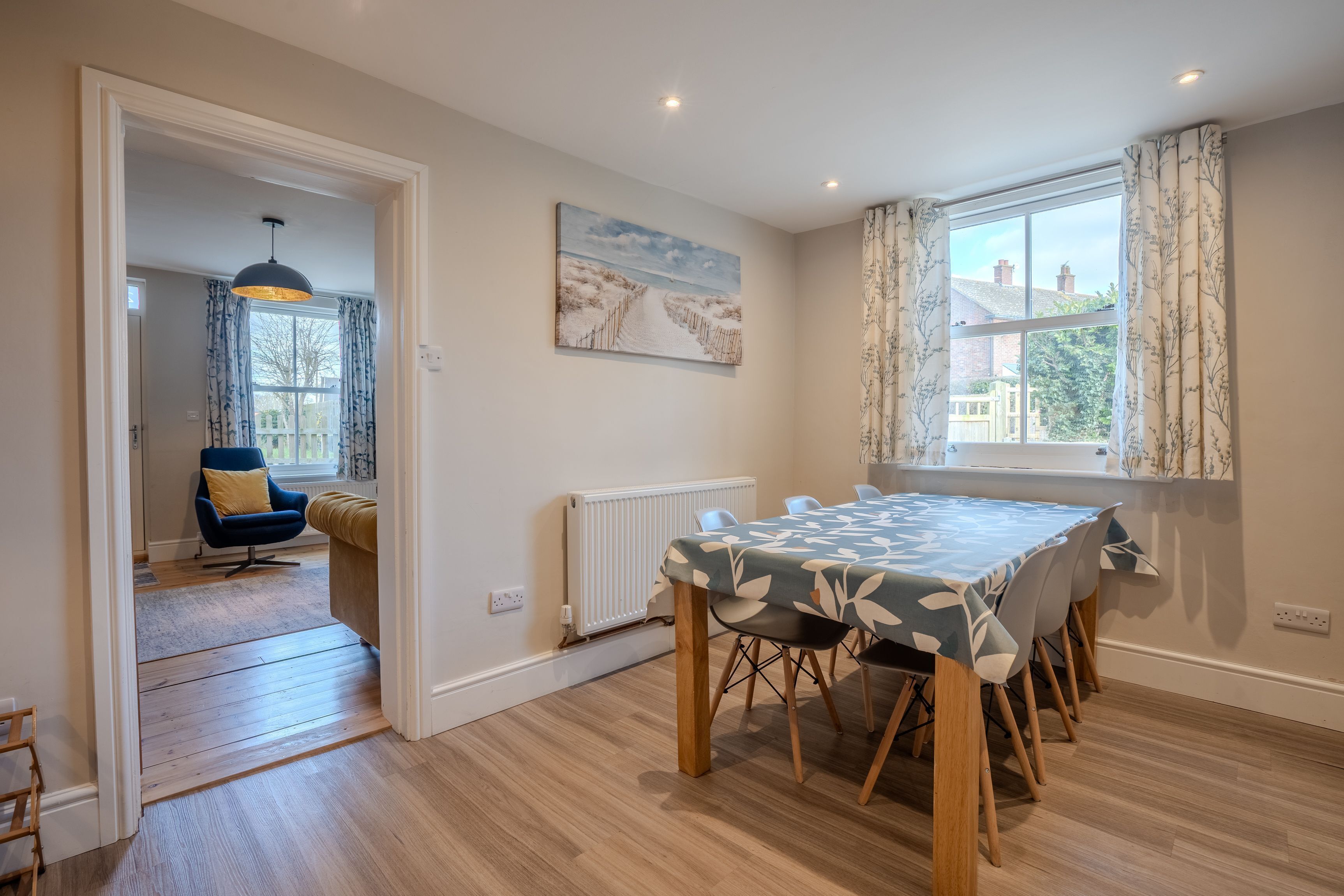 Un comedor con una mesa dispuesta para cuatro, una silla azul, un radiador y una ventana con cortinas.