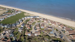 Vista aérea de uma área residencial costeira com casas, uma praia e céu claro.