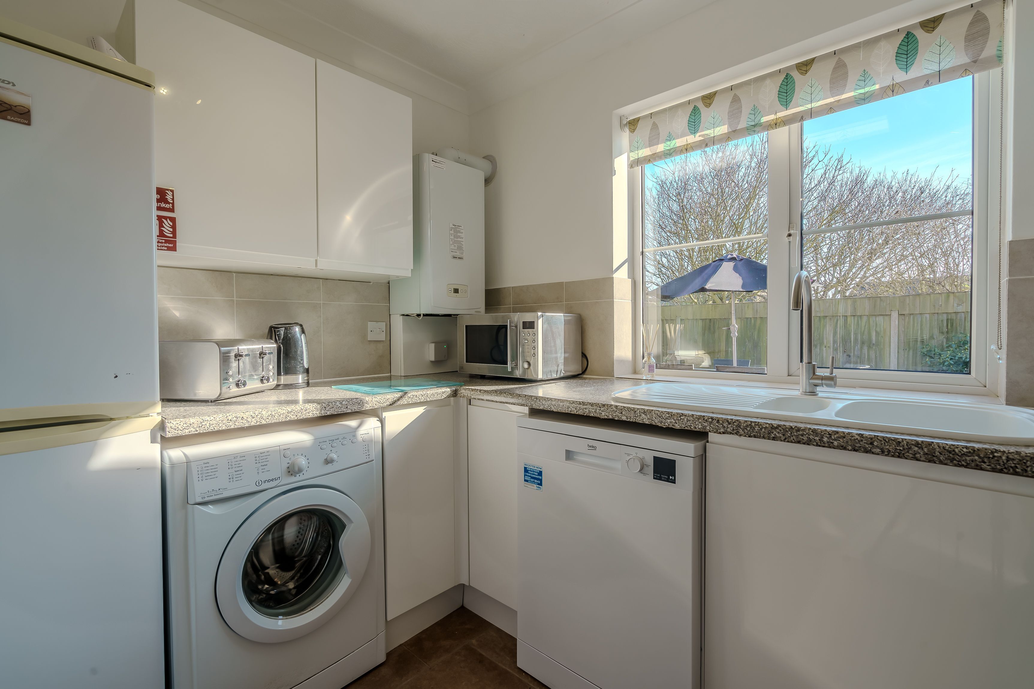 A compact kitchen with a washing machine, microwave, and a window with a view of trees.