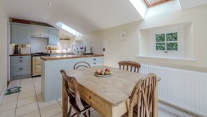 A modern kitchen with a central island, wooden dining table, and chairs. - Sunny Cottage by East Ruston Cottages (Southrepps)