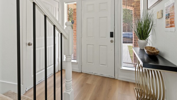 A hallway with a white door, a staircase with black railings, and a wooden floor.