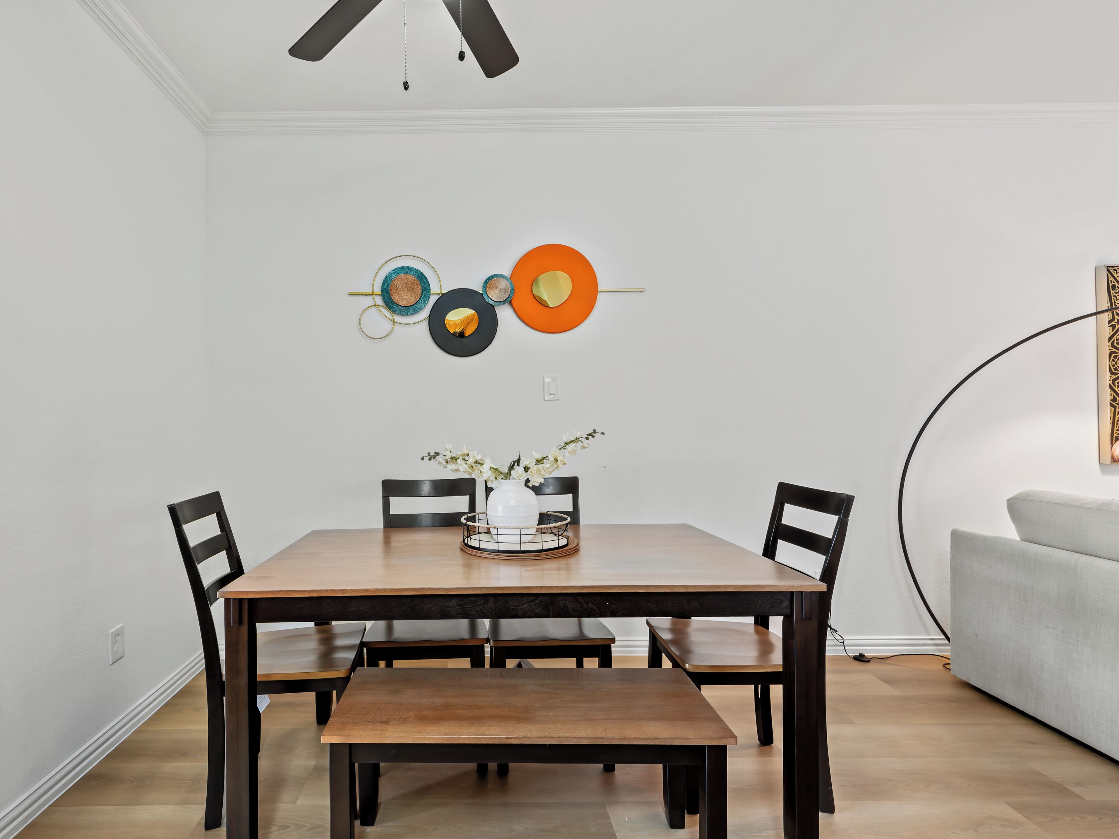A dining area with a wooden table, black chairs, and a bench. There are decorative wall art pieces above the table.