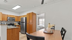 A modern kitchen with wooden cabinets, a stainless steel refrigerator, and a dining area with a wooden table and chairs.