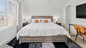 A bedroom with a bed, two bedside tables with lamps, a ceiling fan, a TV, and a chair.