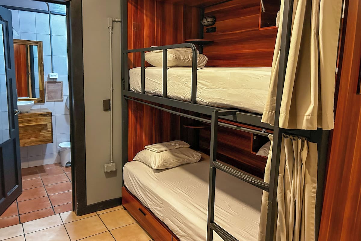 Habitación con literas, cabecera de madera, mesita de noche pequeña y un espejo.