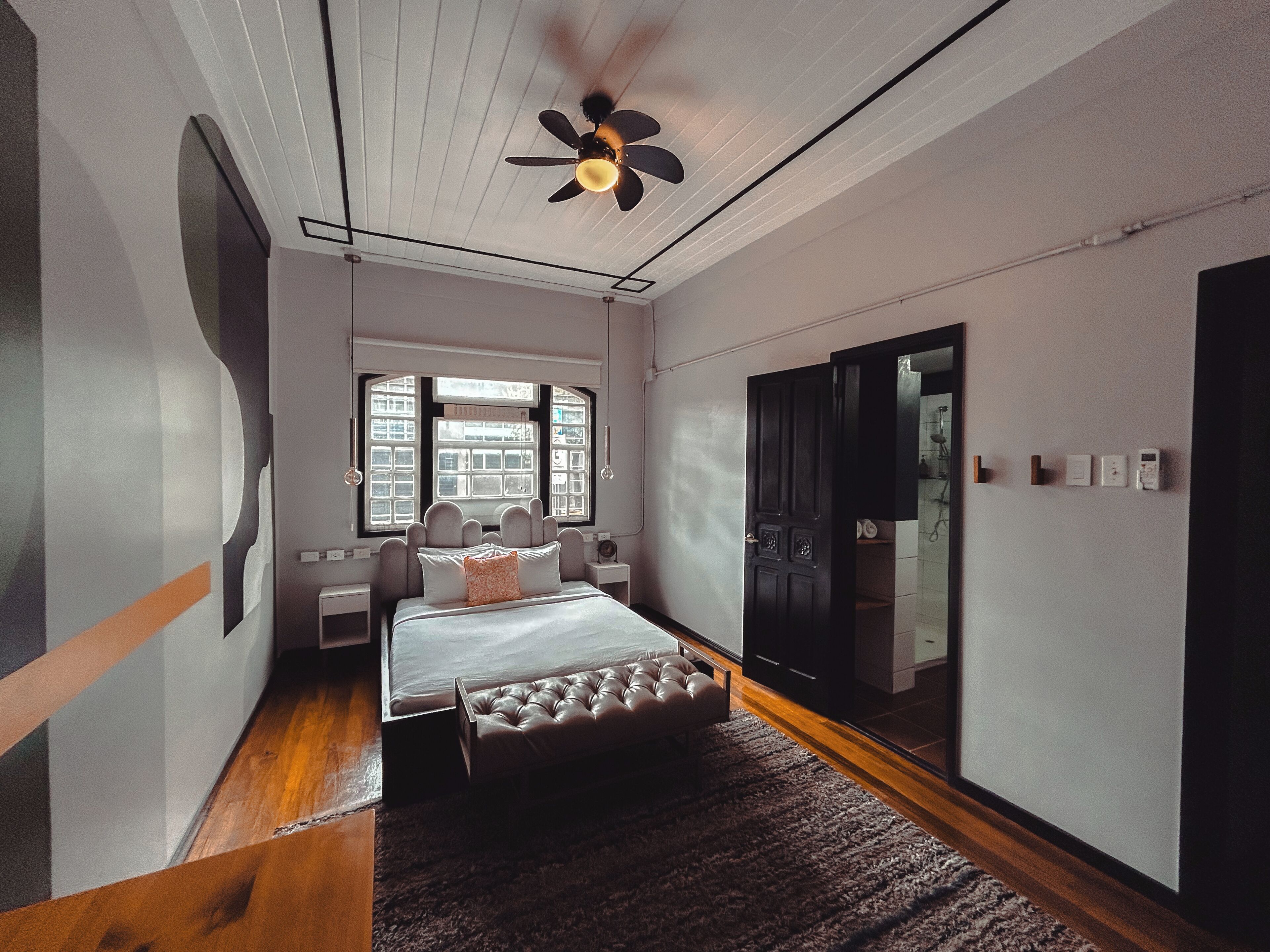 A bedroom with a bed, a ceiling fan, a window, a door, and a bathroom visible through the door.