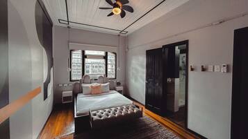 Un dormitorio con cama, ventilador de techo, ventana, puerta y baño visible a través de la puerta.