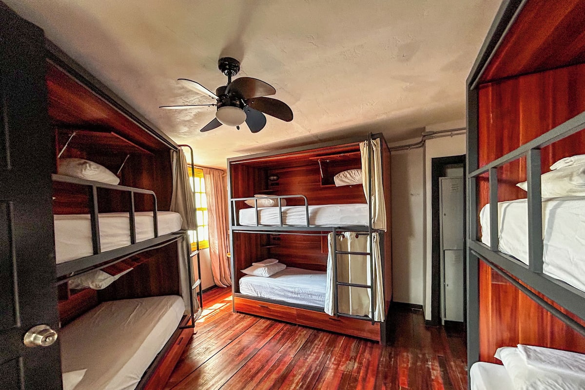 Una habitación pequeña con literas, suelo de madera y ventilador de techo.
