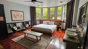 A bedroom with a bed, a desk, two chairs, a ceiling fan, a large window, and a bathroom with a sink and mirror. - Viajero San José Hostel (San José)