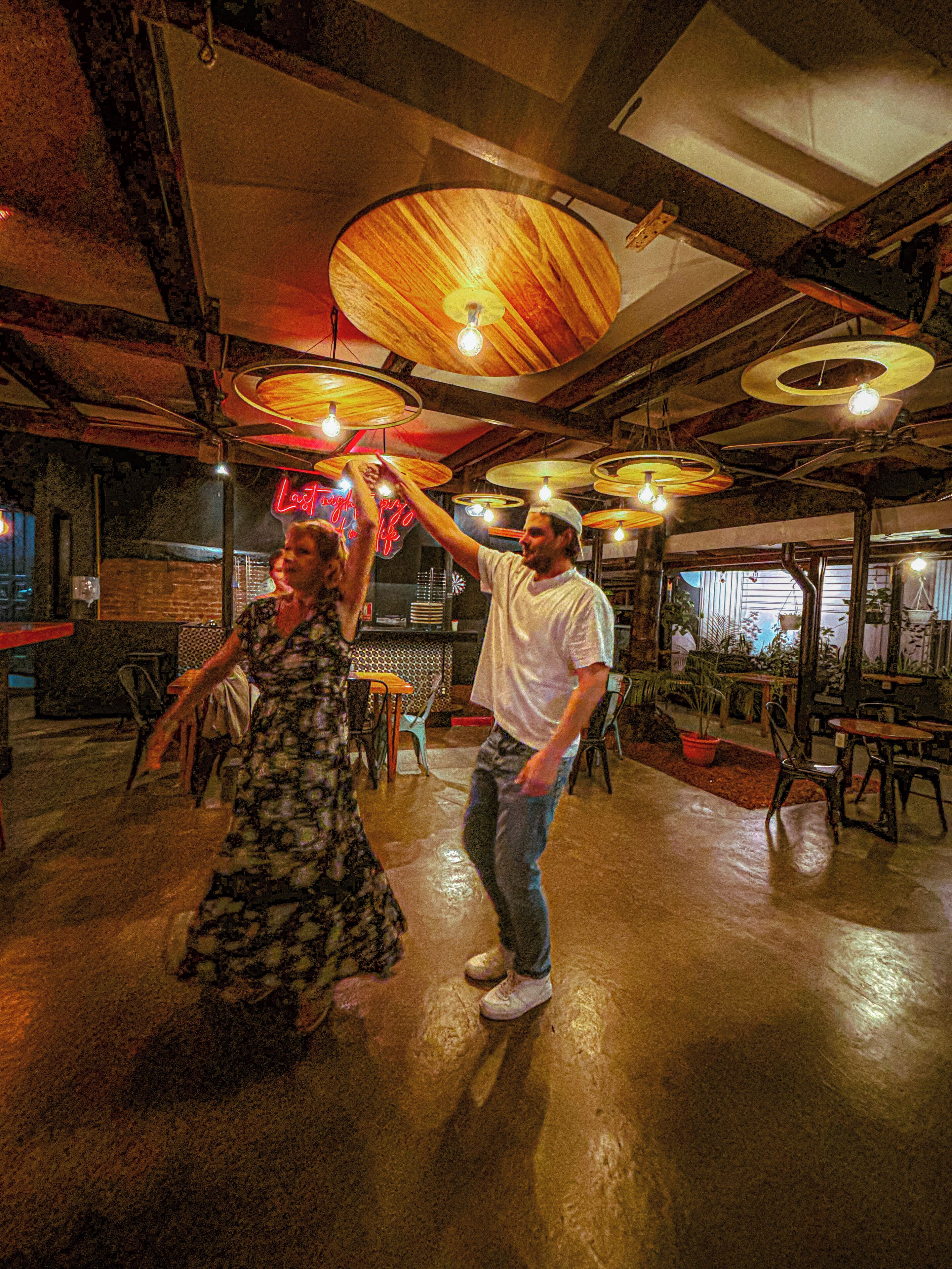 A spacious room with high ceilings and exposed beams, featuring a dance floor with a wooden floor and several tables and chairs.