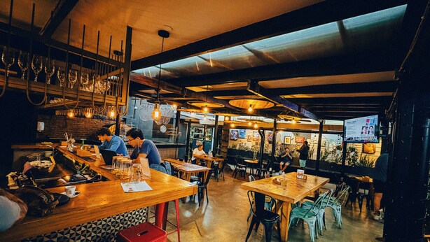 A restaurant interior with wooden tables and chairs, a bar area, and a menu board. - Viajero San José Hostel (San José)