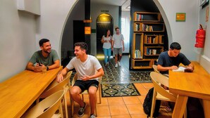A communal area with wooden tables and chairs, a central archway, and a bookshelf filled with books. - Viajero San José Hostel (San José)