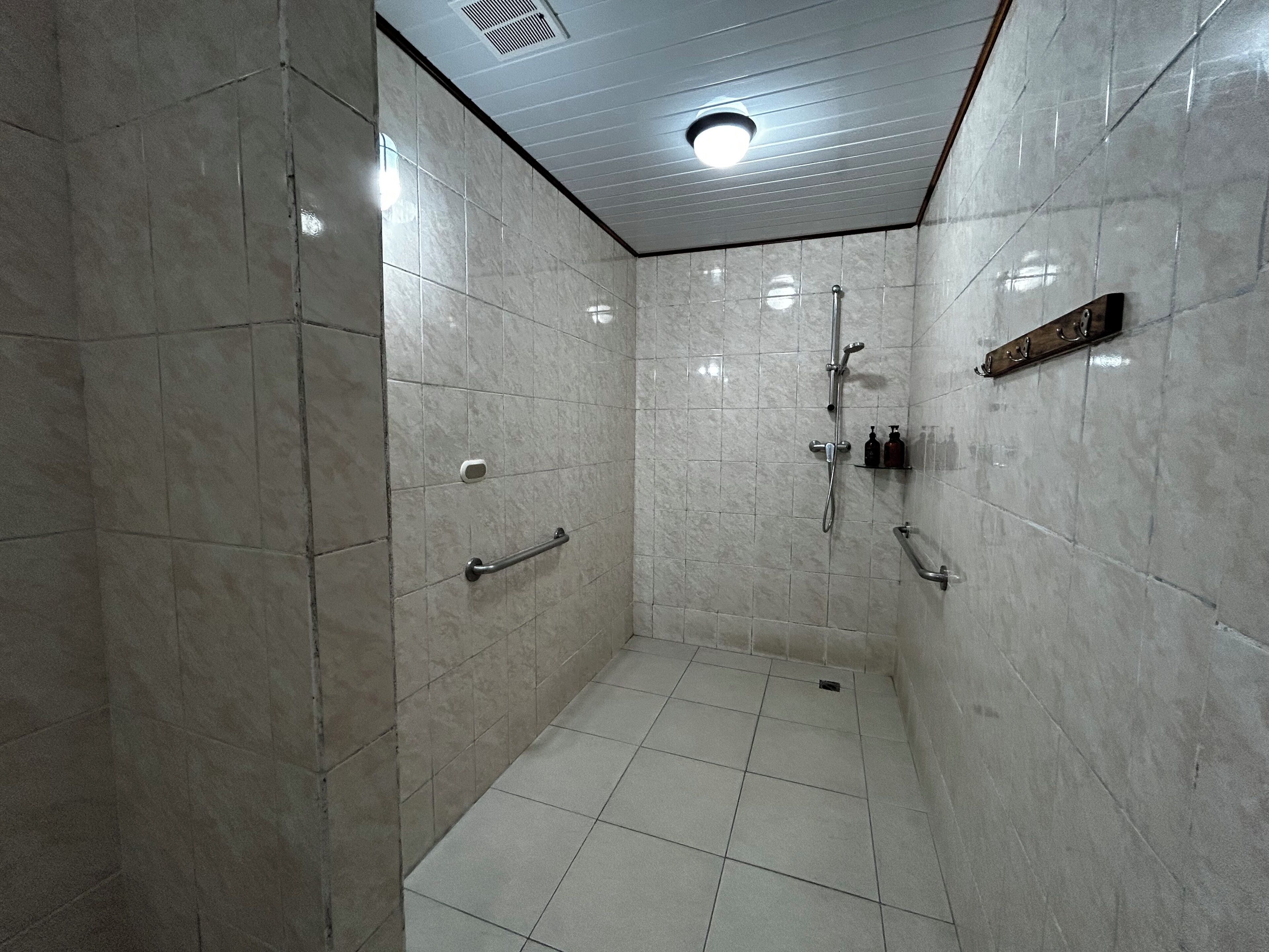 Área de chuveiro revestida com azulejos, com chuveiro manual e torneira fixada na parede.