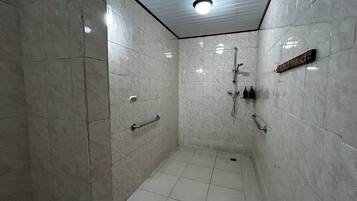 Área de chuveiro revestida com azulejos, com chuveiro manual e torneira fixada na parede.