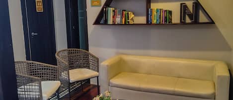 A cozy living area with a sofa, two wicker chairs, a coffee table with a vase, a bookshelf, and a door with a book exchange sign.