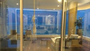 Un interno moderno con un divisorio in vetro, pavimento in legno e un'area salotto con divani e un tavolino.