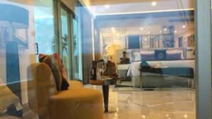 Camera d'albergo moderna con un letto grande, una zona salotto con una poltrona e un tavolo, e vista attraverso una porta in vetro.