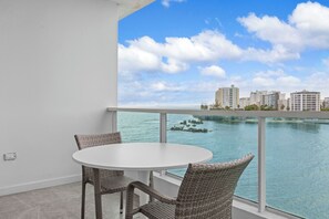 A balcony with a round table and wicker chairs, overlooking a body of water and buildings. - Condado Lagoon by Otium (San Juan)