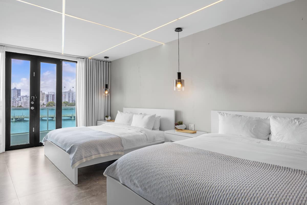 A modern hotel room with two beds, a city view, and a balcony.