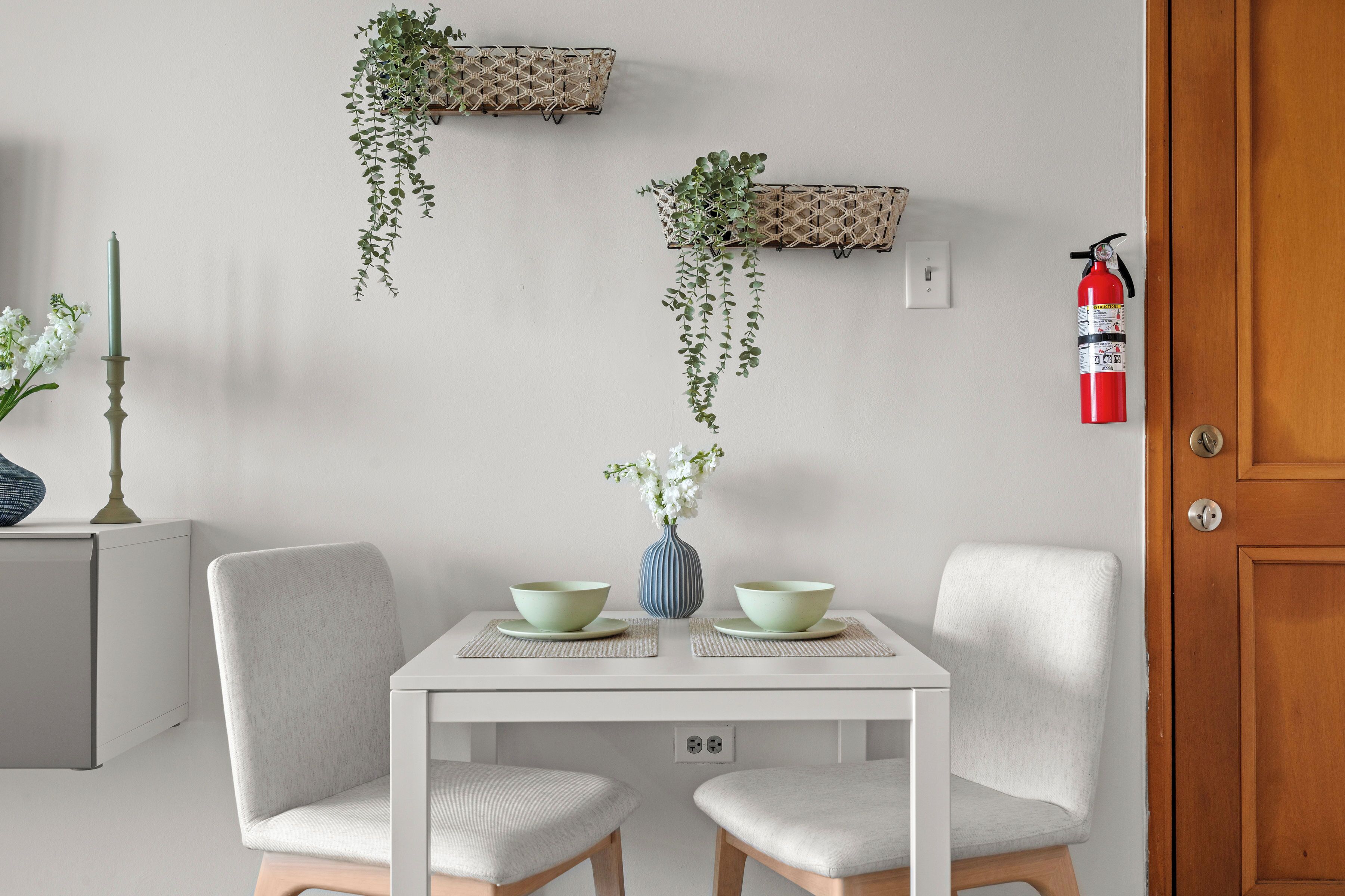 A dining area with a white table, two chairs, a vase with flowers, and hanging plants on the wall.