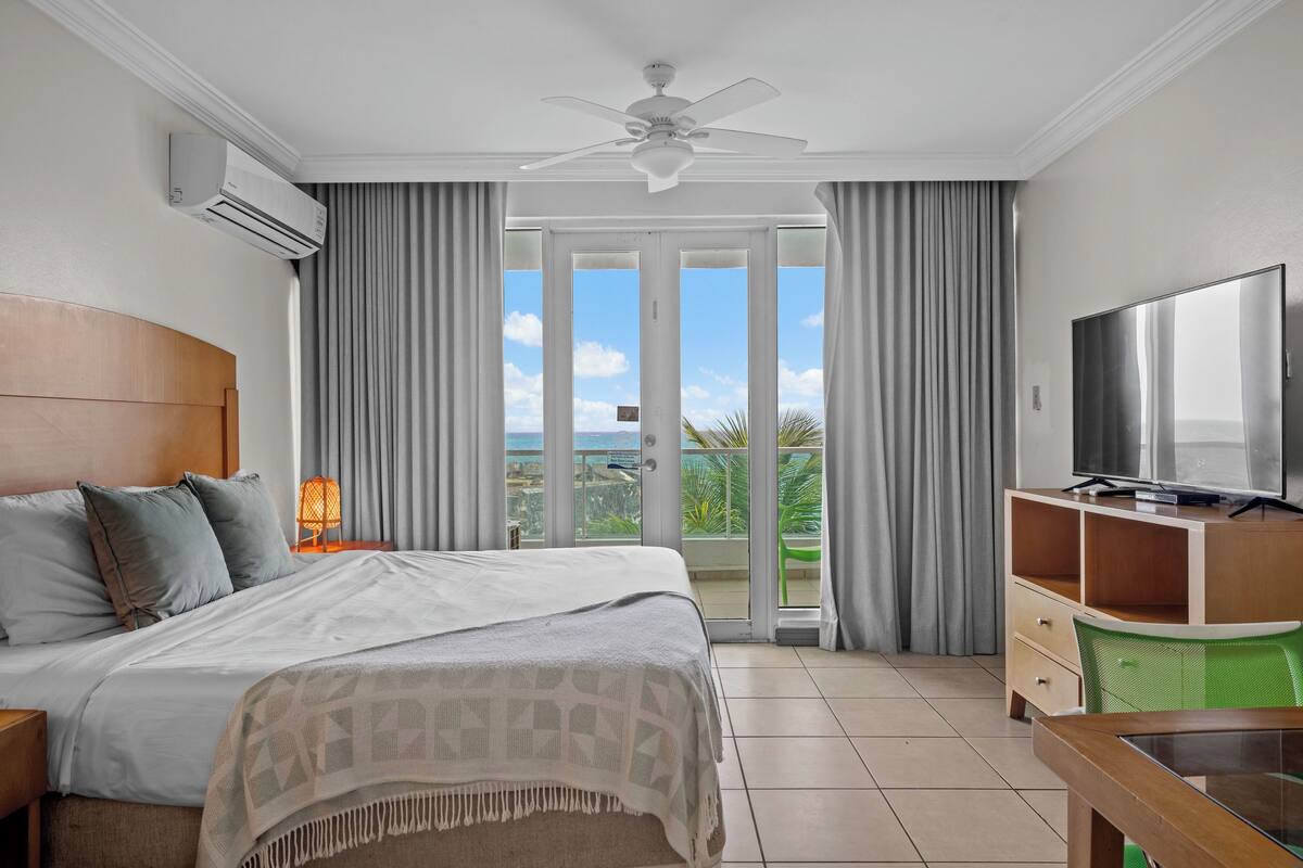 A hotel room with a bed, a TV, a desk, and a balcony with a view.
