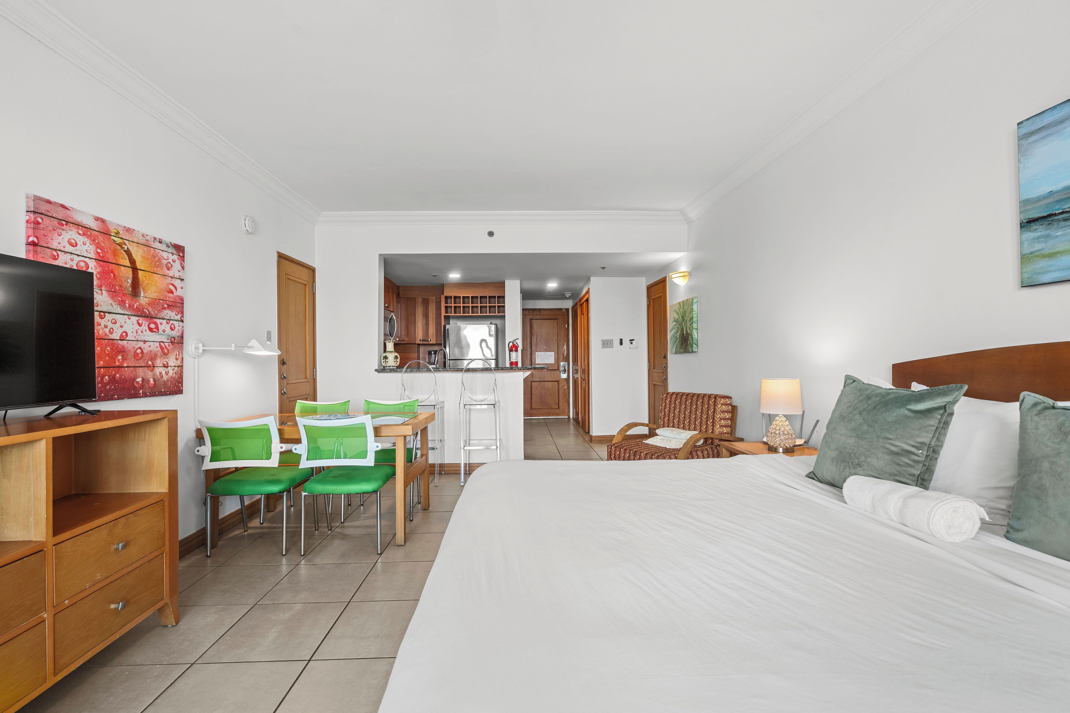 A hotel room with a bed, a desk, chairs, a television, and a kitchen area.