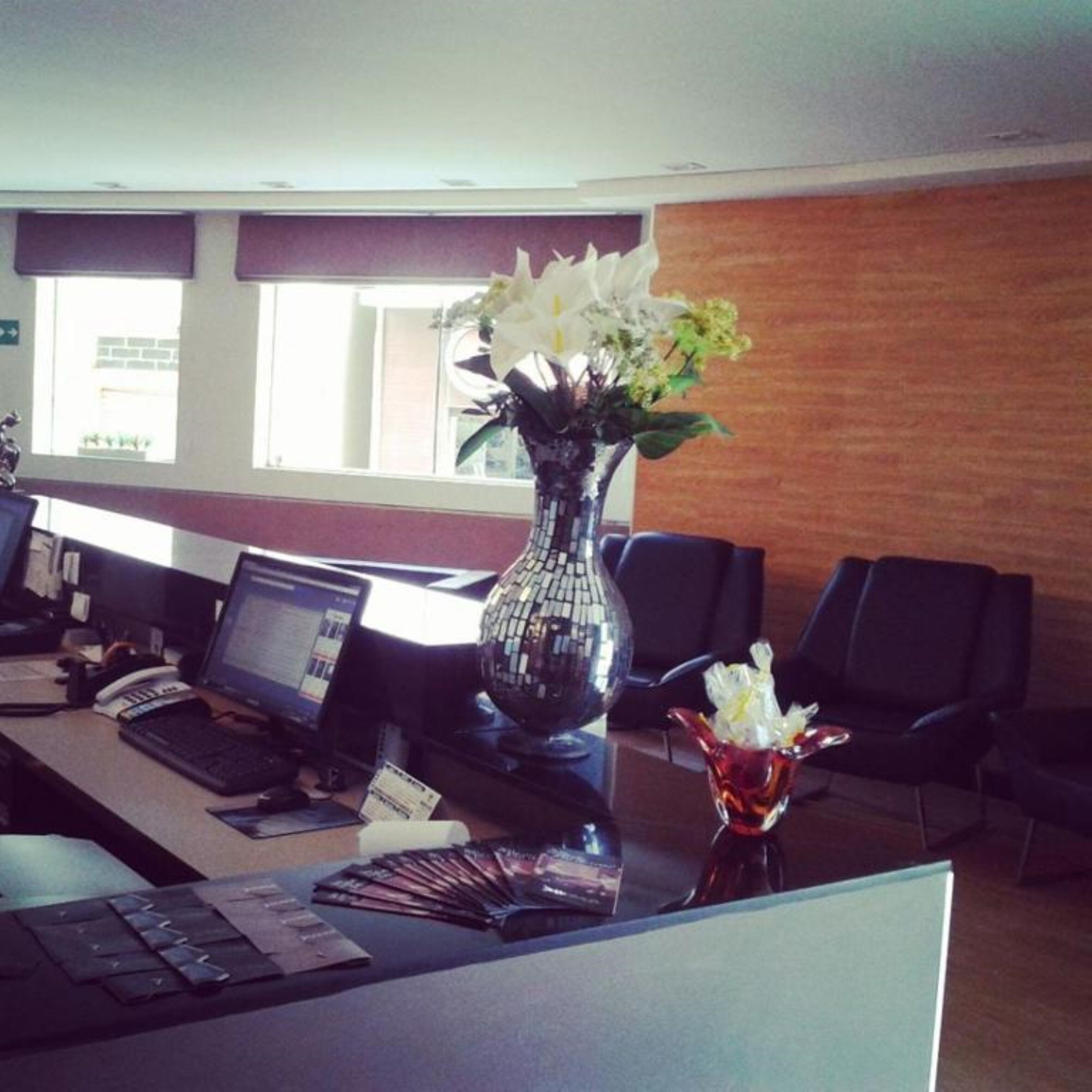 Uma mesa de recepção com um vaso de flores, um laptop e um telefone.