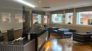 Un área de recepción moderna con mostrador, zona de estar y amplios ventanales con vistas a la calle.