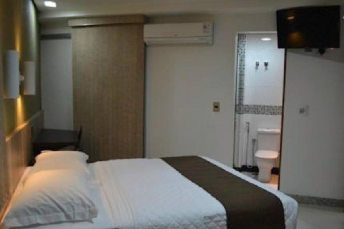 A hotel room with a bed, a TV mounted on the wall, and a bathroom visible through an open door.