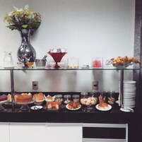 Disposição de buffet com diversos alimentos, um vaso de flores e uma tigela de vidro decorativa.