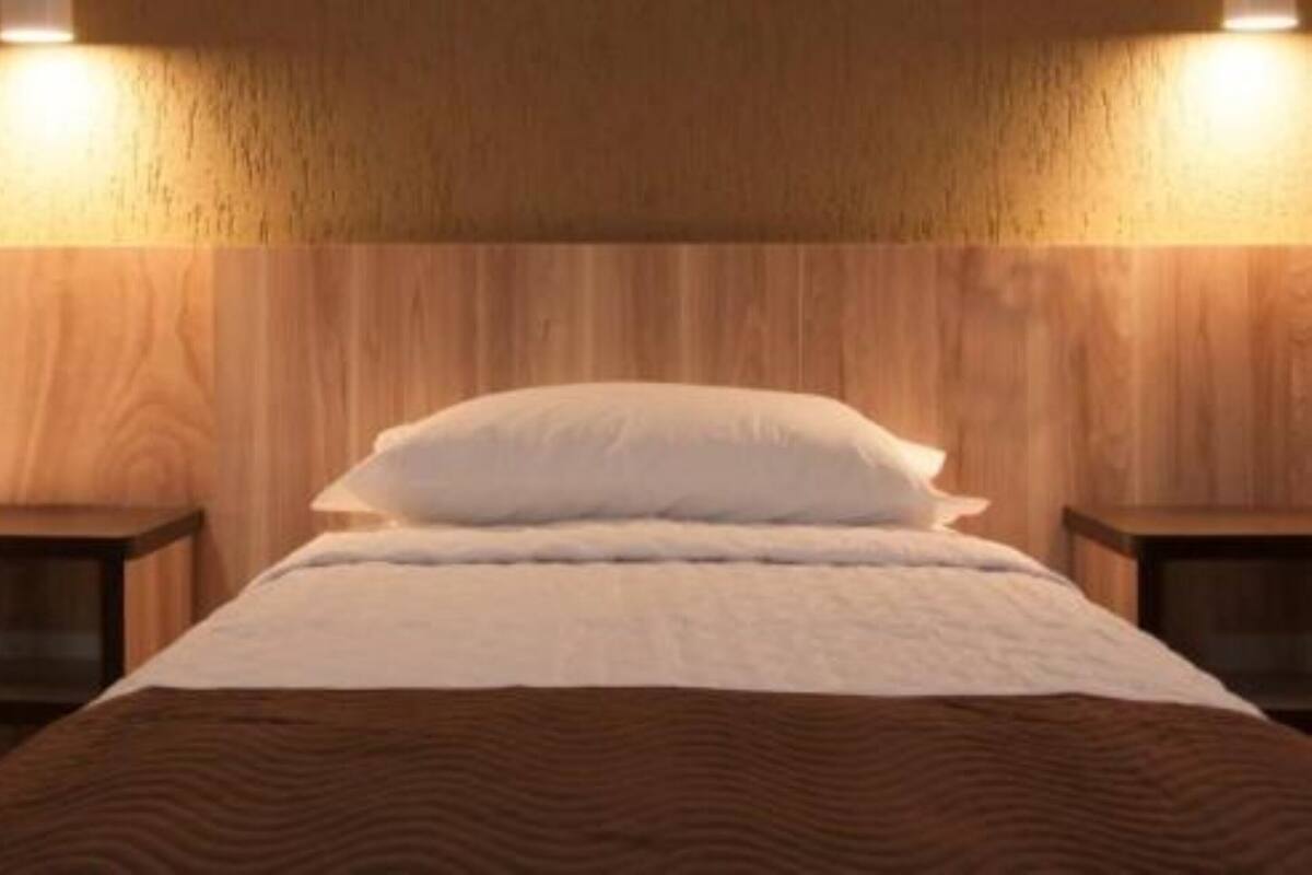 A hotel room with two beds, wooden headboard, bedside tables, and wall-mounted lighting.
