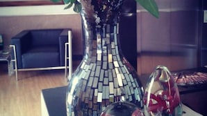 Una habitación con un gran jarrón de mosaico de espejo, un globo de vidrio con una figurita y un sofá azul.