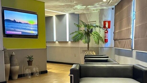 Un área de descanso moderna con asientos de cuero negro, un televisor de pantalla plana mostrando una vista panorámica y una planta en maceta.