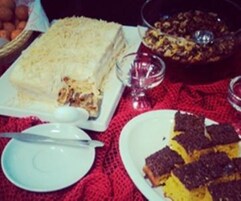 Uma mesa com um bolo retangular grande, uma tigela de frutas e um prato com sobremesa.