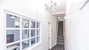 Un couloir avec un escalier, des murs blancs et un lustre.